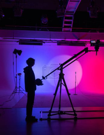 Foto de Una silueta de cinematógrafos emerge frente a un dramático telón de fondo púrpura y rosa, elaborando la historia visual. Detrás del escenario. - Imagen libre de derechos