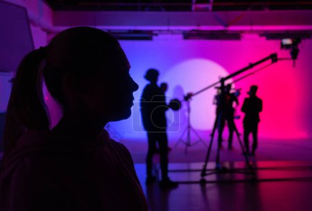 Téléchargez les photos : Profil de silhouette d'une actrice contemplative, immergée dans l'éclairage coloré du studio, avant que la caméra ne roule. Coulisses. - en image libre de droit