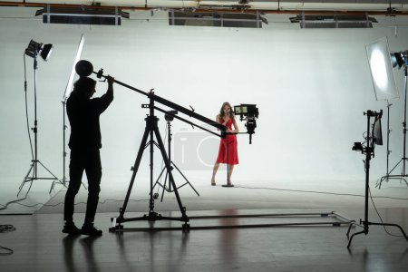 Téléchargez les photos : Equipe de tournage en silhouette capturant une actrice dans une robe rouge frappante sur un plateau de cinéma professionnel. Coulisses. - en image libre de droit