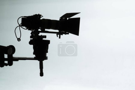 The stark silhouette of a professional film camera and equipment on a bright studio backdrop evokes the essence of filmmaking.