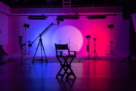 Foto de Silueta de una silla de directores y equipo de cine con luces de neón púrpura y rosa que iluminan el fondo. Detrás del escenario. - Imagen libre de derechos