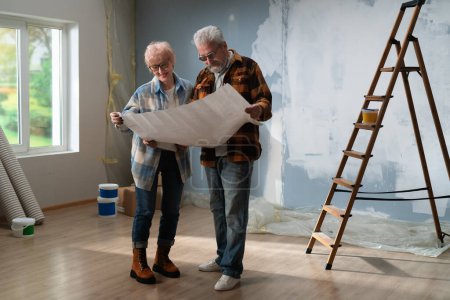 Absorto en la discusión, una pareja de ancianos examina los planes de la casa durante su proyecto de renovación.
