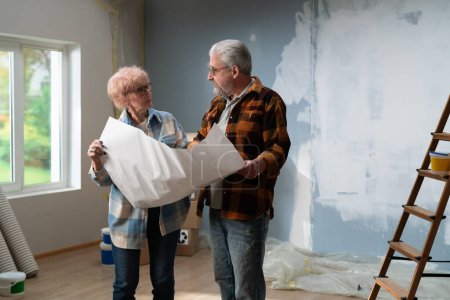 Engrossi dans la discussion, un couple de personnes âgées examine les plans de la maison pendant leur projet de rénovation.