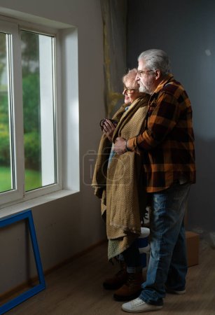 Foto de Una pareja envuelta en una manta mira por la ventana, abrazando los cambios durante las renovaciones del hogar. - Imagen libre de derechos