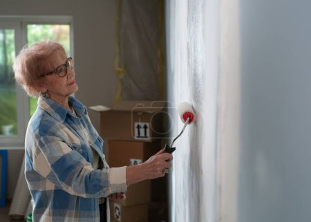 Foto de Una anciana enfocada está inmersa en el proceso de pintar las paredes de su hogar. Vista lateral. - Imagen libre de derechos