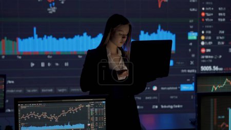 Photo for Financial corporate business concept. Successful business person in the office. Woman investor ceo top manager in front of big digital screens with stock exchange charts working on laptop. - Royalty Free Image