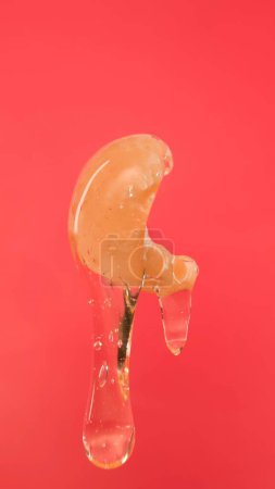 Photo for Thin trickle of amber honey pours and covers cashew nut on red background. A close-up of a nut watered with sweet pulling honey. The concept of healthy tasty food. - Royalty Free Image