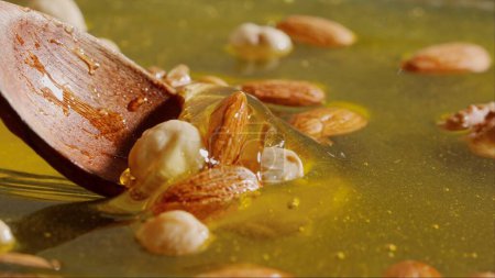 Healthy organic honey with nuts. Wooden spoon scooping sweet fresh golden honey with almonds, walnuts and hazelnuts in the thick syrup, close up shot.