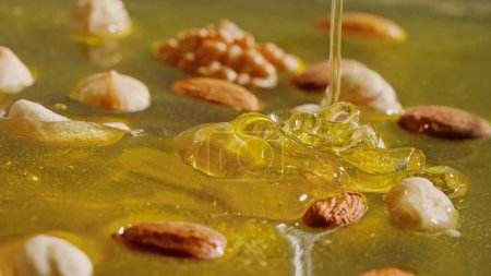 Téléchargez les photos : Miel bio sain aux noix. Miel d'or frais sucré avec des amandes, des noix et des noisettes dans le sirop épais dégoulinant du haut, gros plan. - en image libre de droit