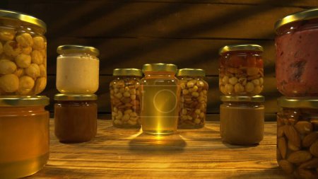 Foto de Miel orgánica saludable con nueces. Muchos frascos de vidrio en la mesa de madera de dulce miel dorada fresca con almendras, nueces y avellanas en el jarabe grueso, tiro de cerca. - Imagen libre de derechos