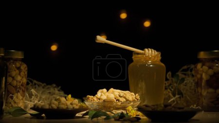 Foto de Miel orgánica saludable con nueces. Frascos de vidrio de pie sobre la mesa de madera con miel dorada fresca, cazo de miel puesta en el frasco abierto en el jarabe grueso, fondo oscuro. - Imagen libre de derechos