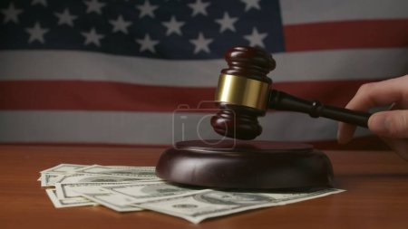 Photo for Man at desk with wooden gavel, dollar bills and US flag in background. A judge in a courtroom, striking with a wooden gavel. Close-up. Court and bribery - Royalty Free Image