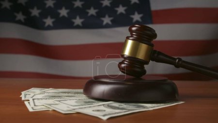 Foto de Un mazo de jueces y billetes de dólar en un fondo de la bandera de los Estados Unidos de América. Un mazo de jueces de madera descansa sobre una mesa. Concepto de juicio, soborno y justicia. - Imagen libre de derechos