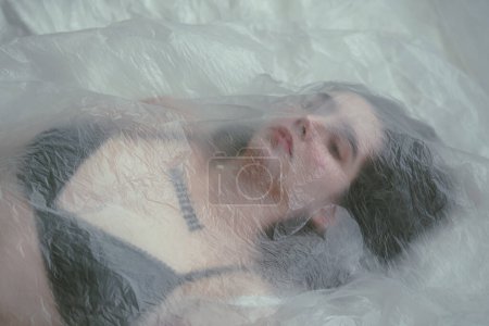 Foto de Retrato de una joven de cabello oscuro, contemplativa mientras yace bajo una sábana translúcida. - Imagen libre de derechos
