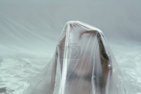 A haunting image of a figure veiled under a sheer sheet, with a distinct tattoo peeking through, evoking a sense of mystery and anonymity.