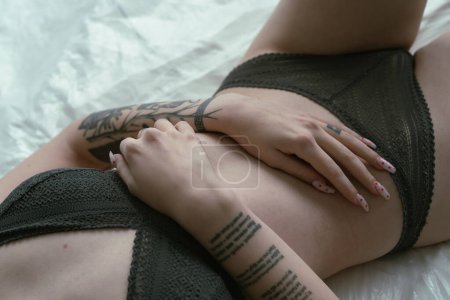 Una joven yace pensativamente en una cama blanca, su cuerpo adornado con intrincados tatuajes, mostrando una mezcla de sensualidad y arte