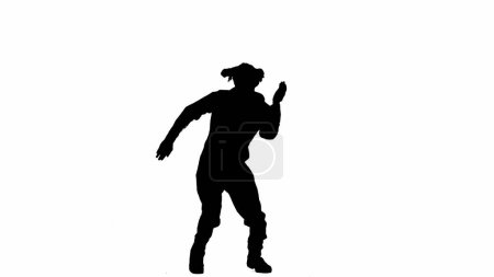Téléchargez les photos : Silhouette noire d'un homme en salopette dansant joyeusement. Un homme méconnaissable aux cheveux bouclés pose sur un fond blanc isolé - en image libre de droit