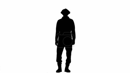 Téléchargez les photos : Une silhouette noire d'un homme en salopette fixe avec confiance la caméra. Un homme méconnaissable aux cheveux bouclés pose sur un fond blanc isolé - en image libre de droit