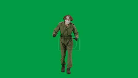 Photo for A maniac in a hockey mask and overalls with a knife in his hand walks and looks around. Unrecognizable man in scary Jason Voorhees look on green screen chromakey. Halloween, horror - Royalty Free Image