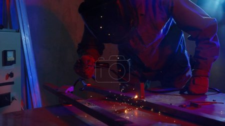 Foto de El proceso de un soldador que trabaja en un producto metálico. Soldador con máquina de soldadura en la superficie de hierro, humo, chispas y luces intermitentes alrededor. Ambiente oscuro con luz azul. - Imagen libre de derechos