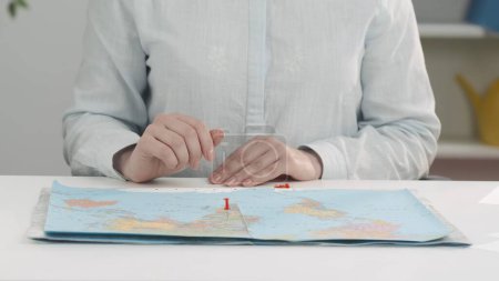 Großaufnahme der Hände einer Reisebüromitarbeiterin, die Orte auf der Weltkarte markiert. Der Prozess der Urlaubsplanung, die Auswahl eines Landes für eine Reise, die Buchung einer Tour, Tickets und Hotels.
