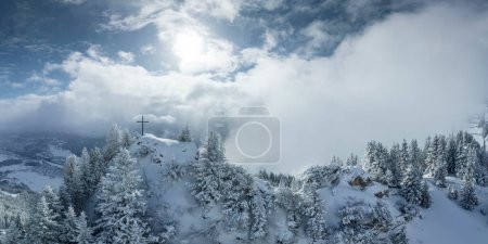 Spectacular summit cross illuminated in the morning sun on the freshly snow-covered Hahnenkamm mountain peak in Austria