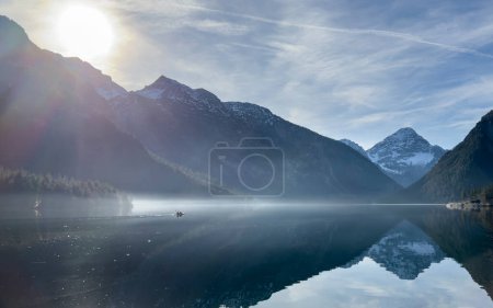 Photo for Beautiful morning mood at lake plansee with a lonely boat driving in the reflection of the mountains in the morning haze - Royalty Free Image