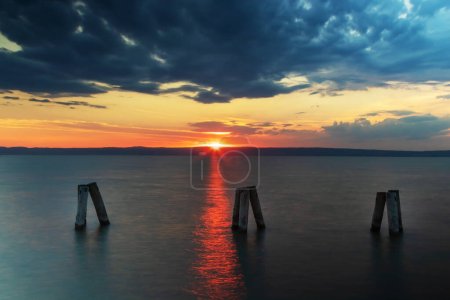 Wooden poles like breakwaters on Lake Neusiedl in Podersdorf, Austria. In the background is a dramatic sky at sunrise.