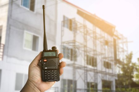 Photo for A portable radio transmitter holding in hand, blurred an outdoor building which is constructioning, soft and selective focus. - Royalty Free Image
