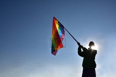 Bandera del arco iris sosteniendo en la mano contra el fondo azul, concepto para la celebración LGBT en el mes de orgullo, junio, en todo el mundo.