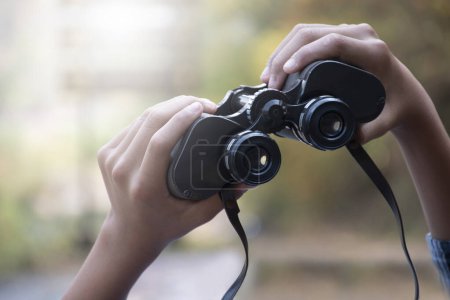Hands holding binoculars, blurred natural background, concept for vacation, observation, trekking, camping, hiking and birdwatching.