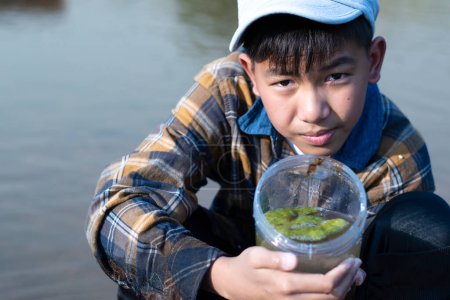 Photo for Asian boy holds transparent plastic tube which contains freshwater algae from river behind him inside, idea for learning water, river, environment, insect, fish, insecticide, pesticide and pollution. - Royalty Free Image