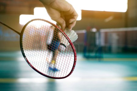 Badminton player holds racket and white cream shuttlecock in front of the net before serving it to another side of the court.