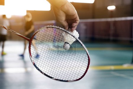 Photo for Badminton player holds racket and white cream shuttlecock in front of the net before serving it to another side of the court. - Royalty Free Image