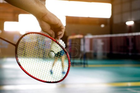 Le joueur de badminton tient une raquette et un volant blanc crème devant le filet avant de le servir sur un autre côté du terrain.