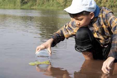 Foto de Colegial asiático sosteniendo tubo de plástico transparente para mantener el agua dulce del río local en el interior para estudiar la fertilidad del agua, el río y los peces y para hacer el trabajo de proyecto de la escuela ambiental fuera de los laboratorios. - Imagen libre de derechos