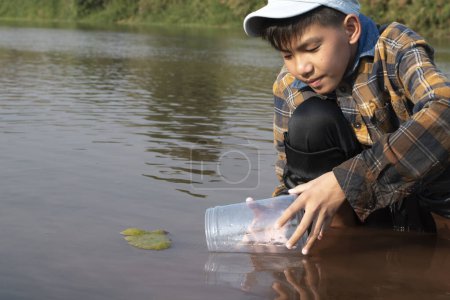 Foto de Colegial asiático sosteniendo tubo de plástico transparente para mantener el agua dulce del río local en el interior para estudiar la fertilidad del agua, el río y los peces y para hacer el trabajo de proyecto de la escuela ambiental fuera de los laboratorios. - Imagen libre de derechos