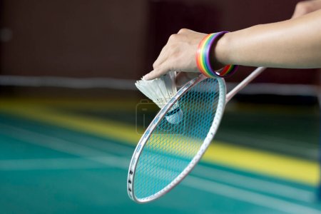 Badminton player wears rainbow wristbands and holding racket and white shuttlecock in front of the net before serving it to player in another side of the court, concept for LGBT people activities.