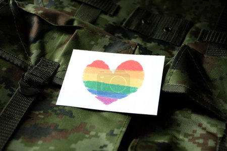 Heart drawing in rainbow colours card on camouflage military backpack, concept for supporting and calling out all people to respect gender diversity of humans and to celebrate LGBTQ+ in pride month