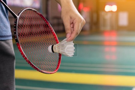 Téléchargez les photos : Le joueur de badminton tient une raquette et un volant blanc crème devant le filet avant de le servir sur un autre côté du terrain. - en image libre de droit