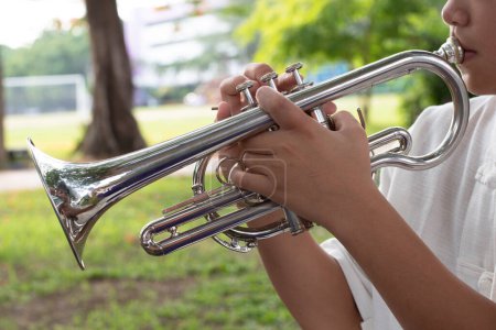 Téléchargez les photos : Instrument de trompette tenant dans les mains d'un étudiant asiatique qui utilise des doigts pour appuyer sur les vales supérieures de la trompette tout en l'apprenant à l'école. Focus doux et sélectif sur les vales et les doigts de trompette. - en image libre de droit