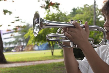 Téléchargez les photos : Instrument de trompette tenu dans les mains d'un étudiant asiatique qui s'entraîne avant de le jouer lors d'une cérémonie en l'honneur du drapeau national le matin. Focus doux et sélectif sur cloche circulaire de trompette. - en image libre de droit