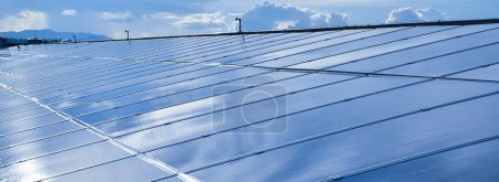 Foto de Photovoltaic or photoelectric rooftop which has the reflection of the Sun and clouds on the surface, cropped shot. - Imagen libre de derechos