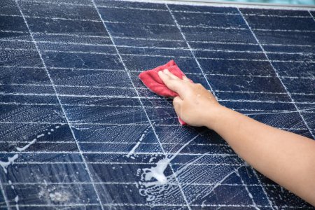 The upper surface of small solarcell panel which is so dirty with dust, birds' feather, rainwater stain, smoke and dirt from birds was cleaning and washing by house's owner, in motion, soft focus.