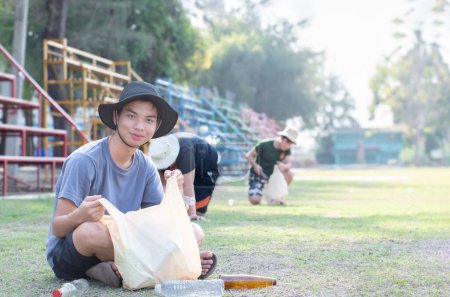 Téléchargez les photos : Préadolescents asiatiques en chapeau et t-shirt faire du bénévolat comme services communautaires en triant les déchets sur le parc local, le nettoyage et le nettoyage de pelouse en séparant les bouteilles en plastique, accent doux. - en image libre de droit
