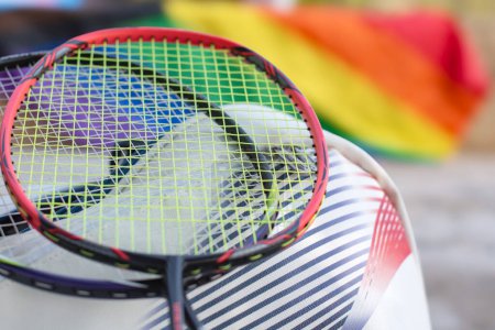 Badminton-Sportgeräte, Schläger und Sporttasche auf dem Boden mit verschwommenem Hintergrund der Regenbogenfahne, Konzept für Breitensport mit allen Geschlechtern und lgbt Menschen auf der ganzen Welt.