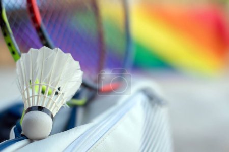 Badminton sport equipments, shuttlecock, rackets in sportbag placed on floor with blurred rainbow flag background, concept for popular sports with all gender and lgbt people around the world.