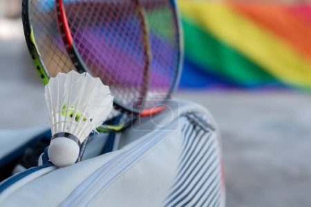 Badminton sport equipments, shuttlecock, rackets in sportbag placed on floor with blurred rainbow flag background, concept for popular sports with all gender and lgbt people around the world.