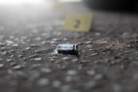 Photo for Pistol bullet shell on cement floor in front of number two yellow paper near car wheel, concept for investigation and crime by using gun, soft focus. - Royalty Free Image