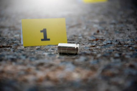 Pistol bullet shell on cement floor in front of number one yellow paper near car wheel, concept for investigation and crime by using gun, soft focus.